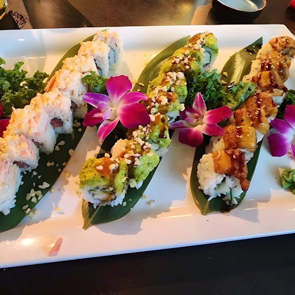 Three rows of sushi rolls, garnished with orchids and greens, on a white rectangular plate.