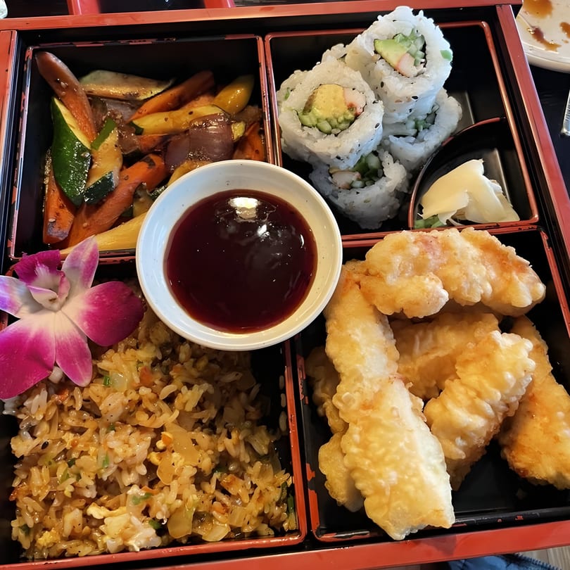 A Rio of Japan bento box with sushi, fried rice, tempura, and stir-fried vegetables.
