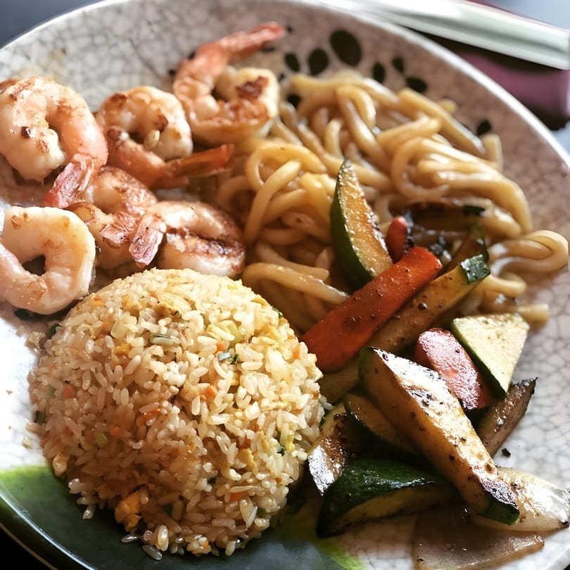 A close-up of a Rio of Japan hibachi plate with shrimp, fried rice, noodles, and grilled vegetables.