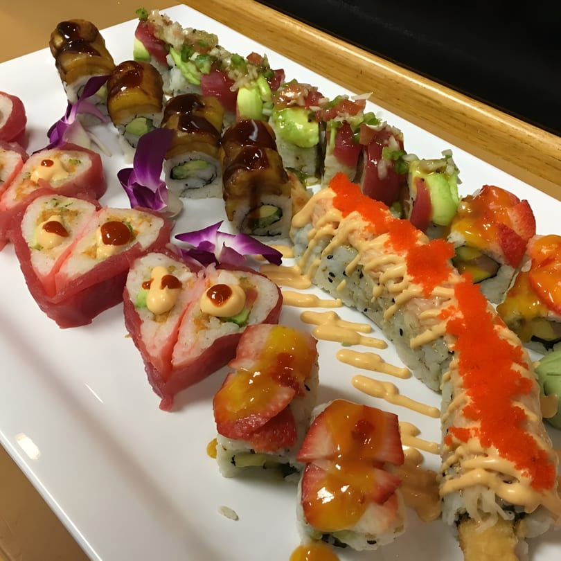 A white platter filled with various colorful sushi rolls, some heart-shaped, with sauces and garnishes.