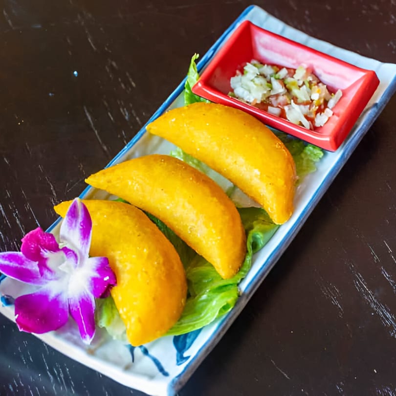 Three golden empanadas on lettuce with a side of salsa and a purple orchid.